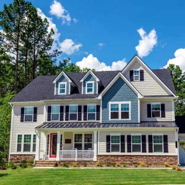 Upscale two-story home featuring a unique blend of tan siding, blue cedar shakes, and a stone foundation, all masterfully finished by Paint It Right.