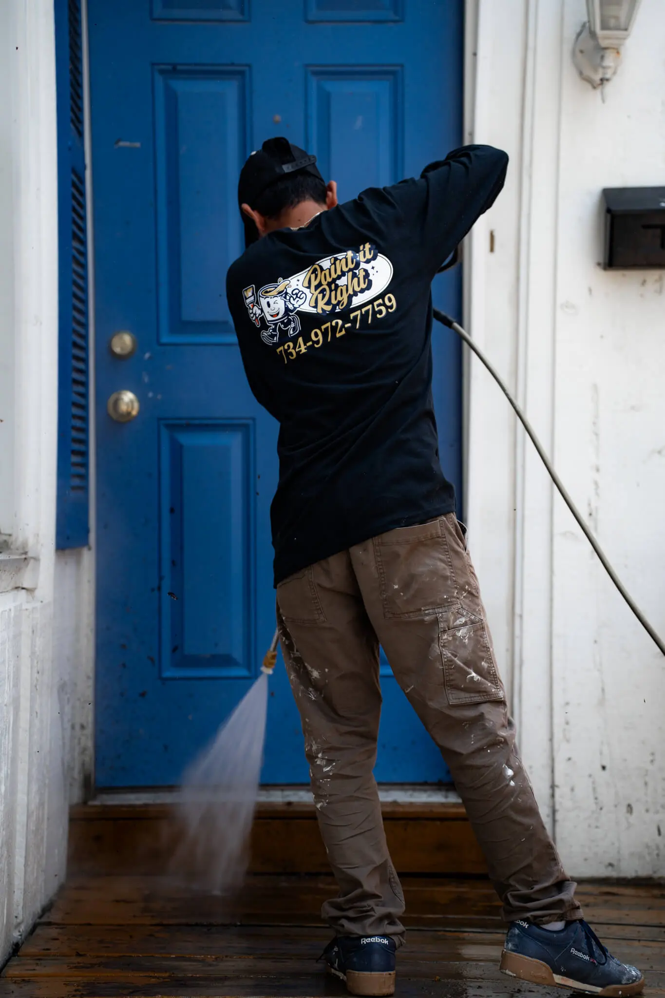 Professional technician from Paint It Right performing high-pressure power washing on a blue residential front door to prepare the surface for a fresh coat of paint.