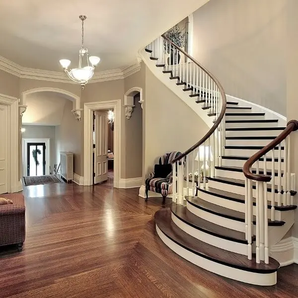 Elegant grand foyer featuring a curved mahogany staircase and classic crown molding, showcasing high-end interior painting in Addison, MI.