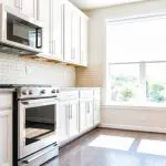 White painted kitchen cabinets with granite countertops and subway tile backsplash in a bright suburban home kitchen.