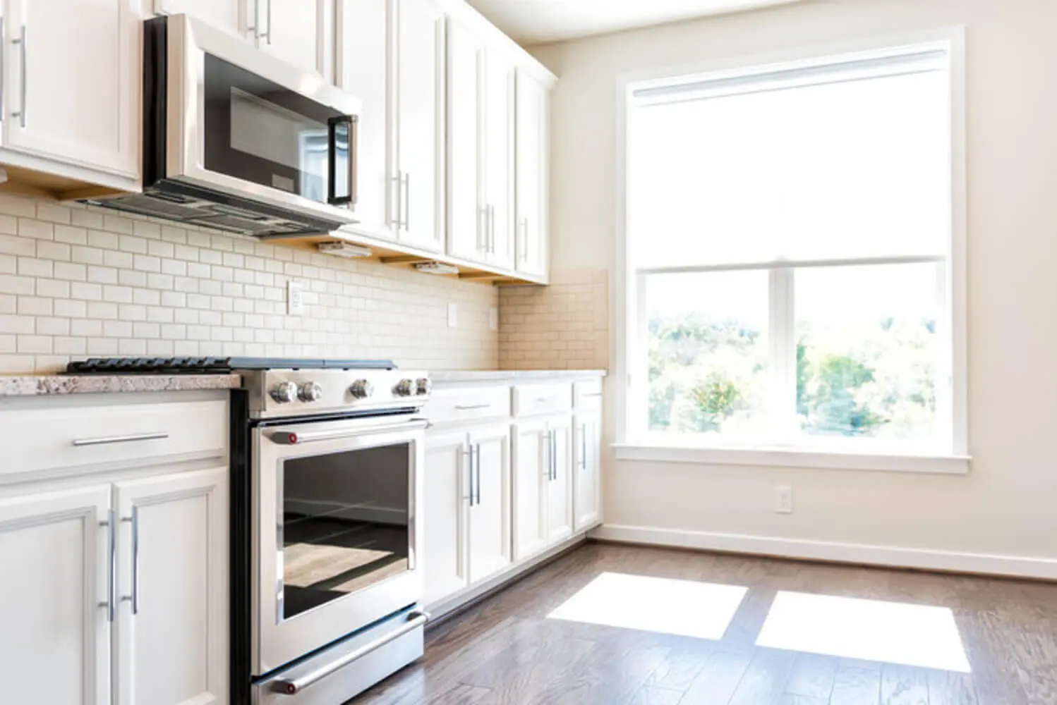 White painted kitchen cabinets with granite countertops and subway tile backsplash in a bright suburban home kitchen.