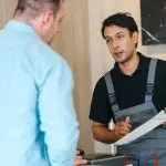 Homeowner listening to a contractor holding a clipboard during an in-home consultation.