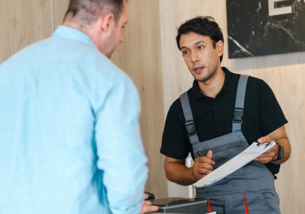 Homeowner listening to a contractor holding a clipboard during an in-home consultation.