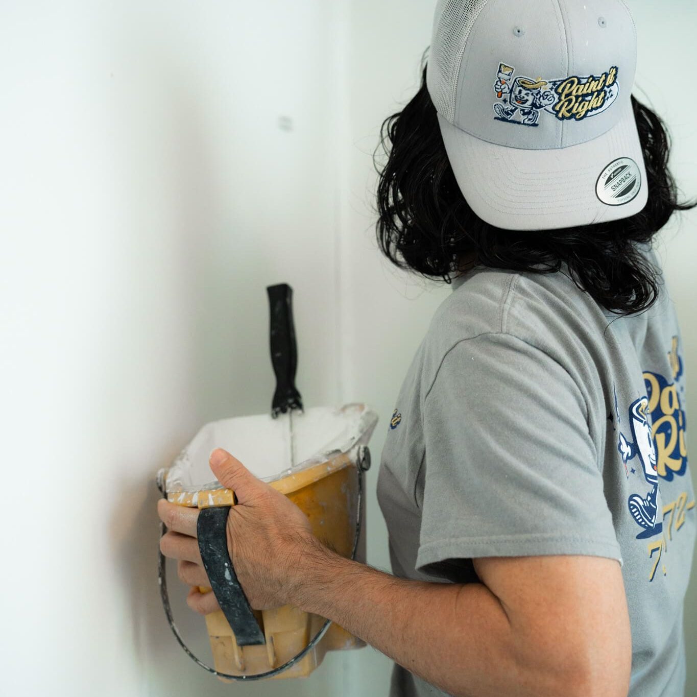 Professional painter in branded gear carefully applying fresh white coating to a corner to Paint It Right.