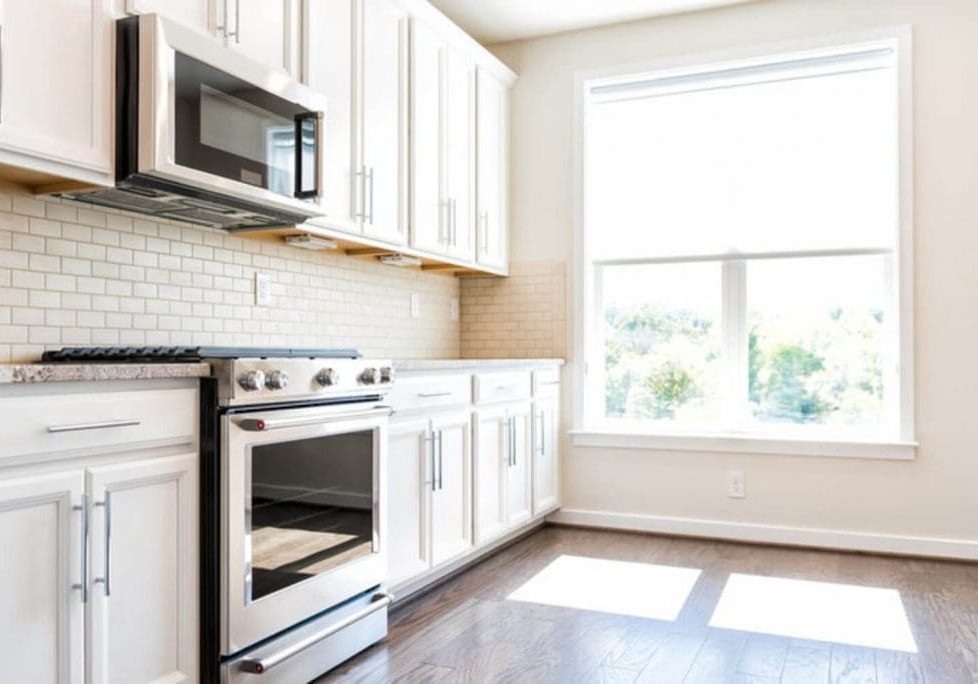White painted kitchen cabinets with granite countertops and subway tile backsplash in a bright suburban home kitchen.